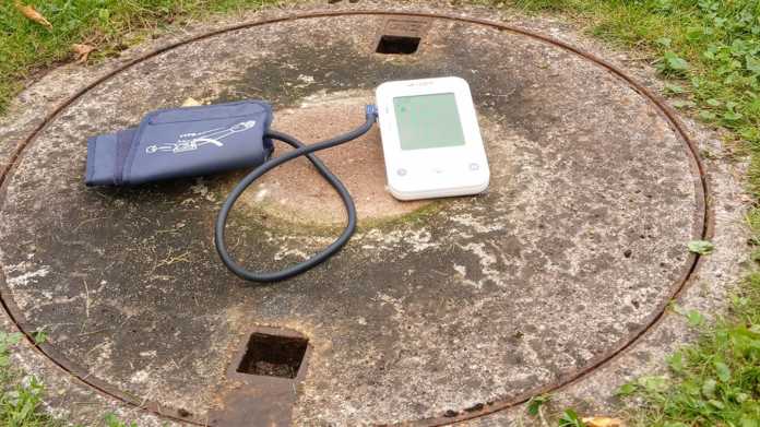 Manhole cover in a meadow with a blood pressure monitor lying on it.