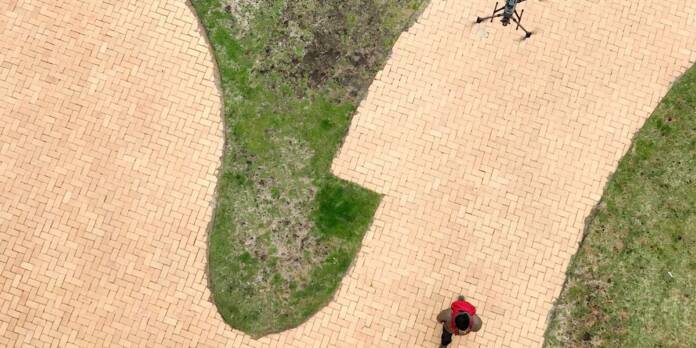 1688106174 overhead view of a brick walkway and man with red backpack walking while a drone is flying in the air.jpg
